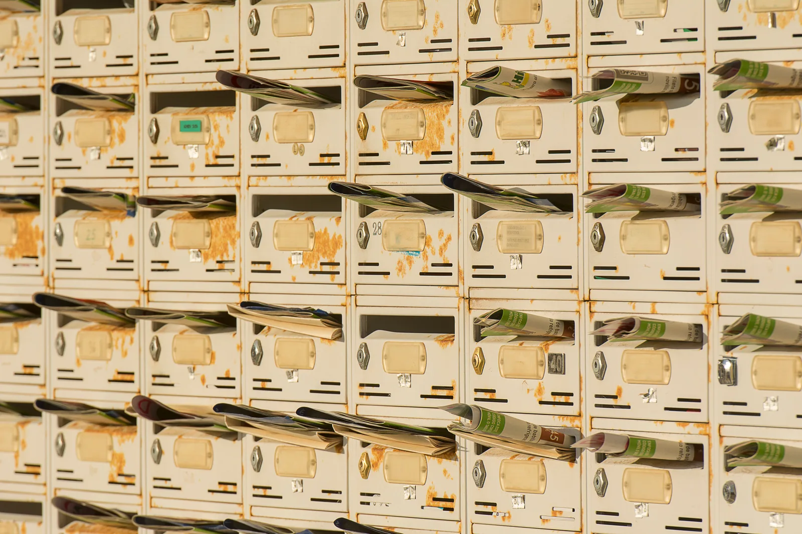 A row of rustic metal mailboxes stuffed with newspapers, creating a vintage urban vibe. Newsletter startup: the operating cycle for new owners