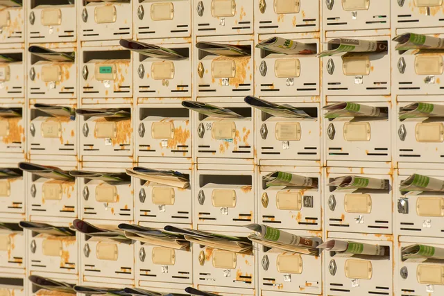 A row of rustic metal mailboxes stuffed with newspapers, creating a vintage urban vibe. Newsletter startup: the operating cycle for new owners